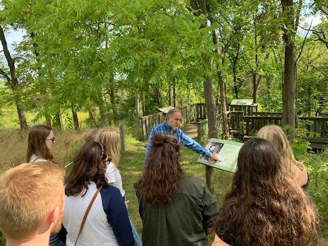 Charlie Fairbank showing a crowd of students an interpretive sign.