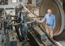 This rig, or powerhouse, is one of six at Fairbank Oil Fields. Charlie Fairbank stands in front of the bullwheel which is two metres in diameter.